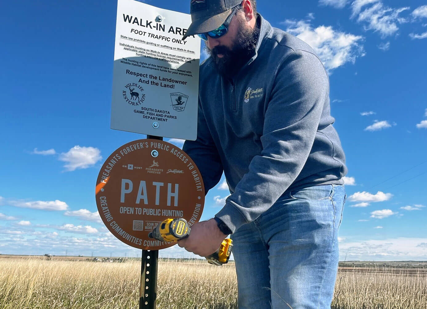 Man installing PATH sign in field with a blue sky